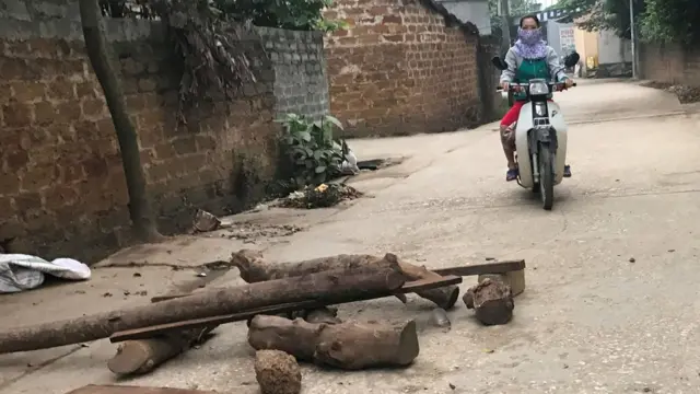 Một phụ nữ đi xe máy trên con đường làng có rải gạch và vài tấm gỗ chắn. Hình chụp ở xã Đồng Tâm, huyện Mỹ Đức, Hà Nội hôm 20/4/2017.