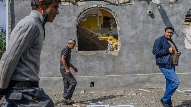 Dağıdılmış evin qarşısından ekçən kişilər