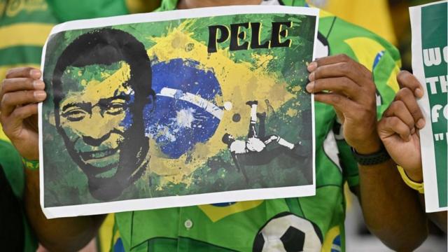 Um homem segurando um cartaz com o rosto de Pelé e a bandeira do Brasil