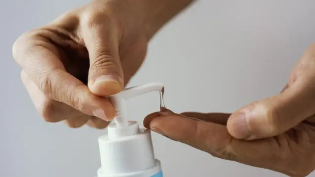 Pessoa apertando frasco de álcool em gel nas mãos