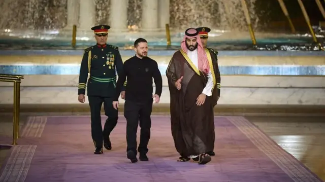 Слева Владимир Зеленский, справа – коронованный принц Саудовской Аравии Мухаммад бин Салман. Они идут по широкой ковровой дорожке светло-пурпурного цвета в сопровождении военных из почётного караула