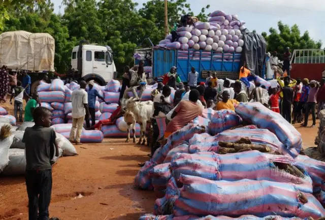 Des personnes chargent les camions avec des cargaisons arrivées du Bénin par bateau pour être transportées vers différentes villes à Gaya, au Niger, le 09 septembre 2023. Suite à la prise de pouvoir militaire au Niger le 26 juillet, certains pays membres de la CEDEAO ont imposé des sanctions et fermé leurs frontières, ce qui a conduit les Nigériens à utiliser différentes méthodes pour commercer avec les pays voisins.