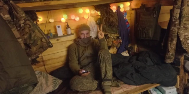 Человек сидит в блиндаже и показывает два пальца, знак победы