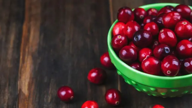 Tigela de louça contendo cranberries sobre uma mesa de madeira