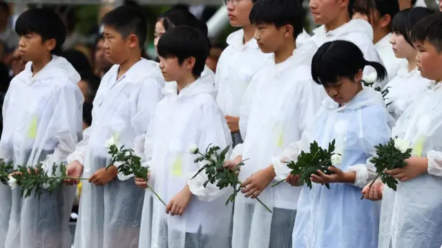 白いビニールの雨合羽を着て白い菊を手にした子供たちが並んでいる