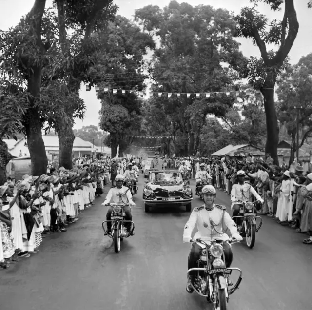 Le général Charles de Gaulle, debout dans sa voiture, est accueilli par la foule à son arrivée à Conakry le 27 août 1958.