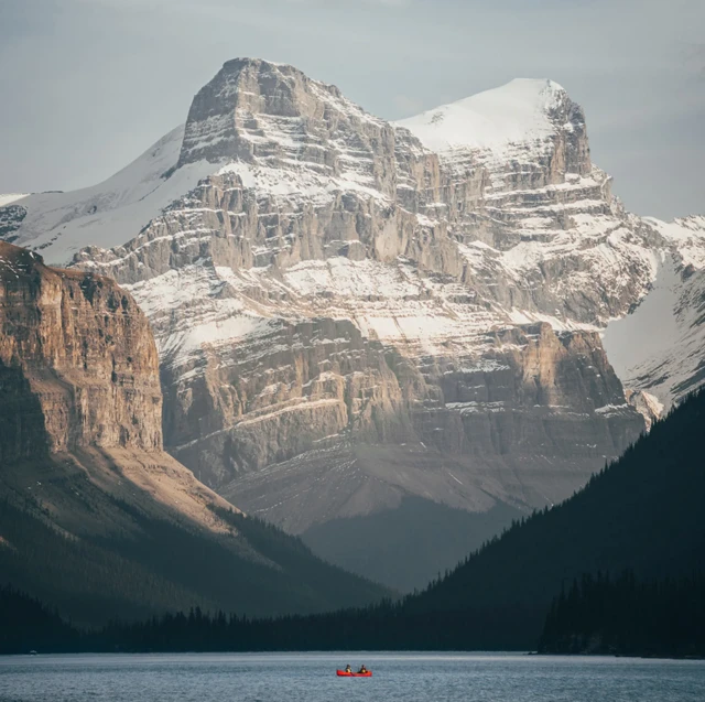 거대한 설산이 호수를 내려다보는 가운데 붉은 카누 한 척이 물 위를 지나간다.