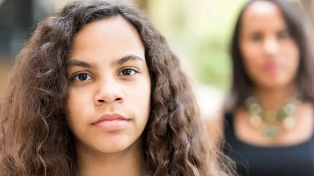 Niña adolescente con madre detrás desenfocada.