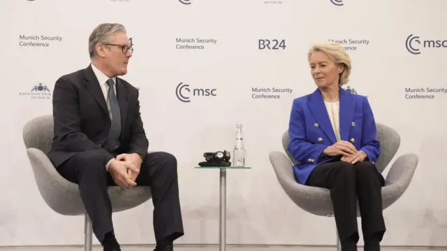 壇上に横並びに置かれた椅子に座り、会談する黒いスーツ姿のスターマー氏と、青いジャケットを着たフォン・デア・ライエン氏。椅子の間に置かれたテーブルには水の入ったボトルなどが置かれている