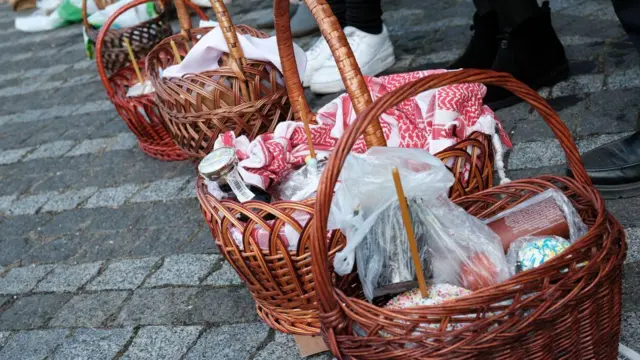 Nekoliko drvenih korpa na pločniku sa uskršnjom hranom, svećama i maramama