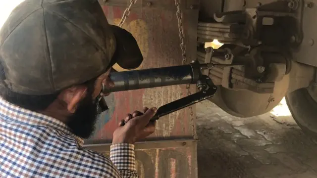 ट्रक के पहियों में ग्रीस लगाता मज़दूर