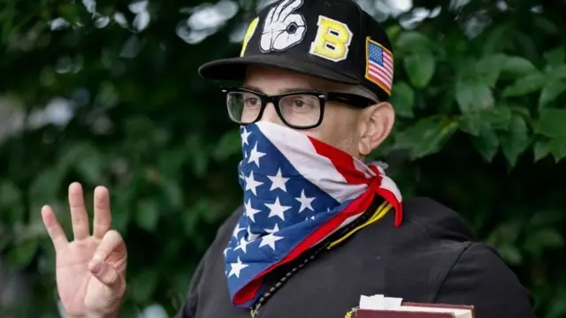 A masked far-right activist does the OK sign during a rally in the US