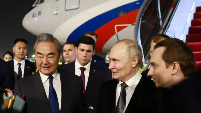 Putin y el canciller chino, Wang Yi, en el aeropuerto, rodeados de otros hombres vestidos de traje y corbata