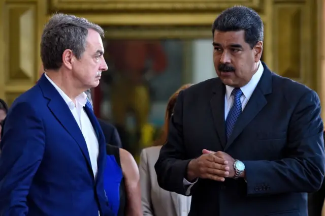 El presidente venezolano Nicolás Maduro (derecha) conversa con el expresidente del gobierno español José Luis Rodríguez Zapatero (izquierda) en el Palacio Presidencial de Miraflores, ambos vestidos de traje, Zapatero sin corbata.