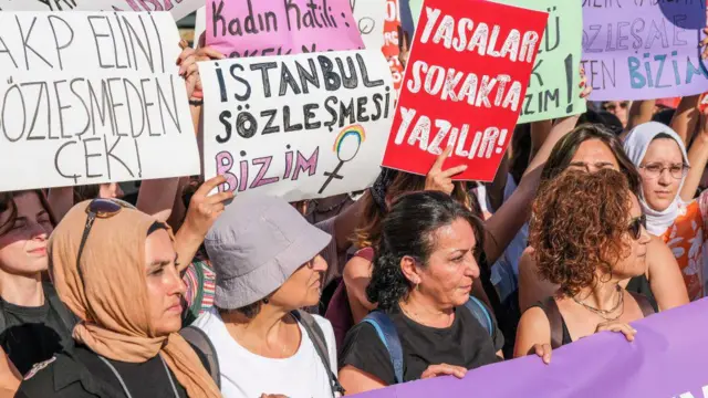 Kadınlar yanyana mor bir pankart taşıyor. Arkadaki dövizlerde "İstanbul Sözleşmesi bizim", "AKP elini sözleşmeden çek" yazıyor.  