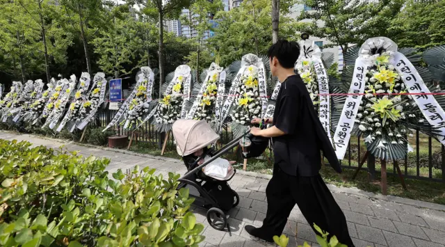 9일 서울 용산구 용산어린이정원 입구에 정부의 용산공원 부지 주택 공급 검토에 반대하는 근조화환들이 줄지어 세워져 있다. 화환 앞으로 검은 유모차를 끌고 가는 한 남성이 보인다.