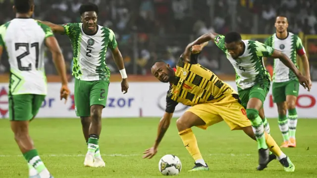 L’attaquant ghanéen Andre Ayew, en maillot jaune et noir, protège le ballon alors qu’il se bat avec un joueur nigérian, en vert et blanc, sous le regard de trois autres joueurs des Super Eagles