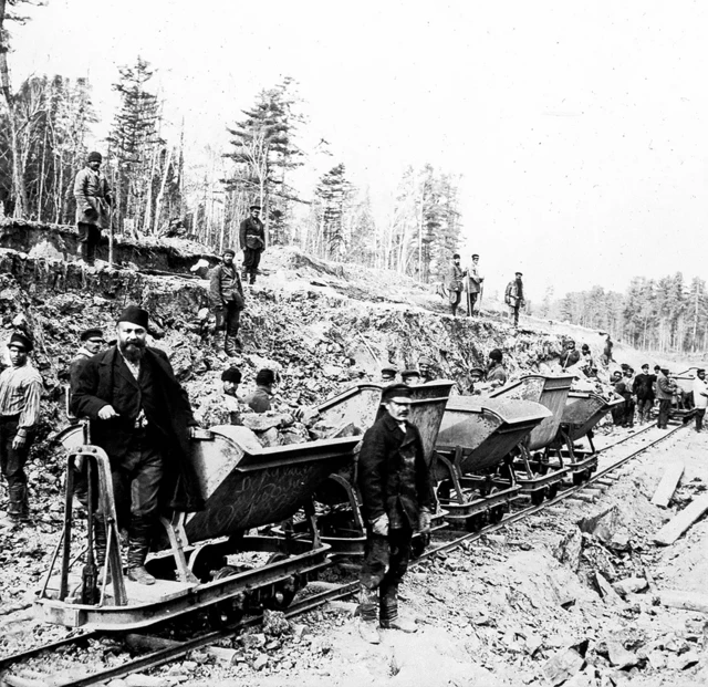 Cette photographie historique illustre la construction du chemin de fer de Sibérie orientale près de Khabarovsk, en Russie, vers 1895. L'image montre des ouvriers manœuvrant de petits wagons basculants pour le terrassement.