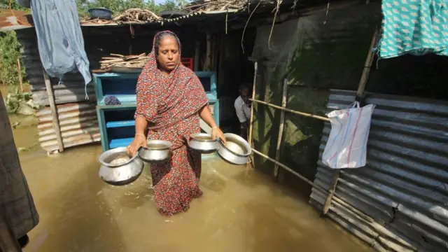 বন্যার পানির মধ্যে সংসারের কাজকর্ম করছেন এক নারী।