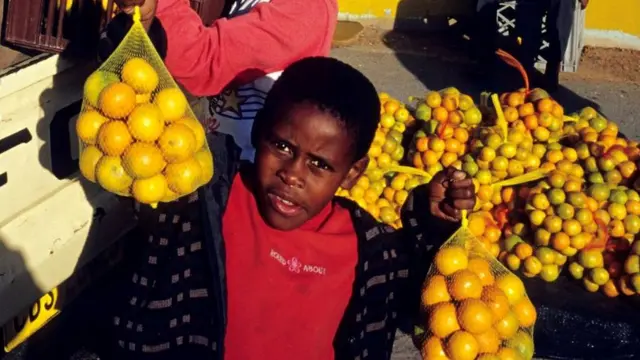 Des enfants non identifiés transportent des oranges depuis une camionnette devant la gare de Nonqubela le 11 août 2001 à Site B Khayelitsha, un township situé à environ 21 miles du Cap, en Afrique du Sud.