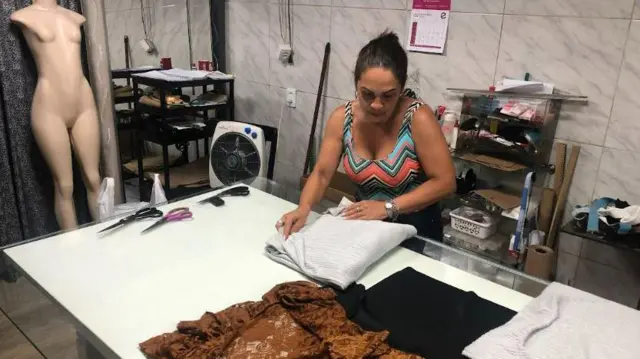 Solange em pé, trabalhando com tecidos em cima de mesa