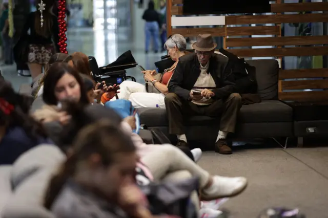 Passageiros sentados aguardam informações sobre seus voos no aeroporto de Maiquetía