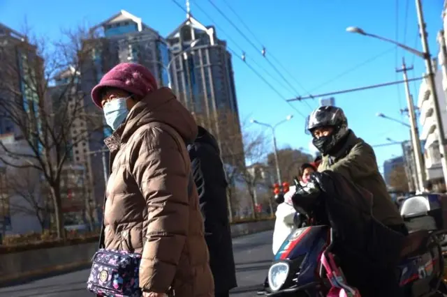 Pekin sokaklarında yolda maskeli bir kadın ve motosiklette bir erkek