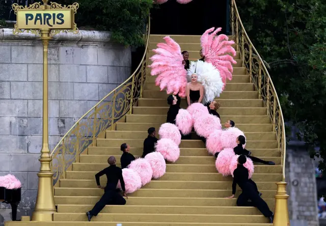 Lady Gaga se produit sur un escalier doré avec des danseurs et des pompons roses lors de la cérémonie d'ouverture à Paris le 26 juillet.