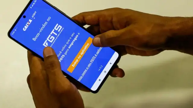 Mãos segurando um celular com o aplicativo do FGTS aberto na tela