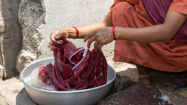 BIJAPUR, INDIA - MARCH 28: A woman in a red sari is washing a cloth in a wash pan while she is sitting in a squat in front of a shack on March 28, 2013 in Bijapur, India. Around 50,000 people are living in the slums who form about one-sixth of the population of Bijapur. (Photo by Christian Ender/Getty Images)