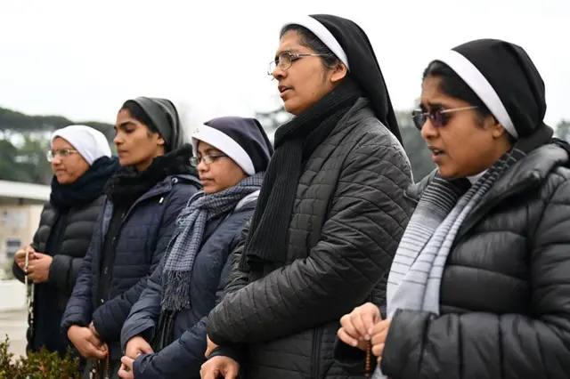 Nuns dey pray in front of di statue of Pope John Paul II outside Rome's Gemelli Polyclinic, wia dem hospitalize Pope Francis on 24 February 2025.