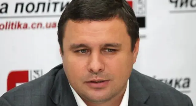 Микитась у сірому жакеті дивиться вниз 