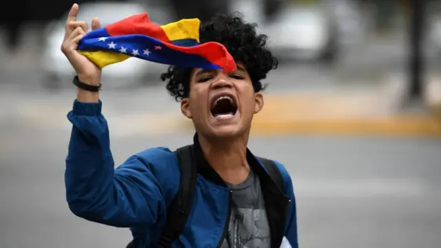 Jovem manifestante grita e segura bandeira da Venezuela