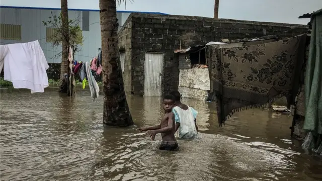 Watoto wanatembea katika barabara yenye mafuriko huku nguo za kulalia zikianikwa ili kukauka