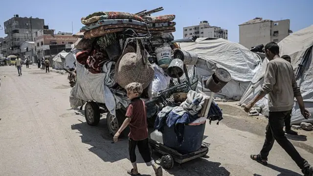 Um menino e um homem adulto caminham ao lado de uma grande carroça, puxada por um cavalo, cheio de pertences na Cidade de Gaza.