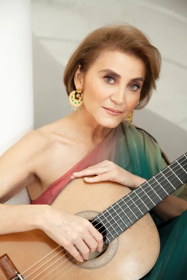 Berta Rojas posa para la cámara. Sostiene una guitarra en sus manos. Tiene una mirada seria. 