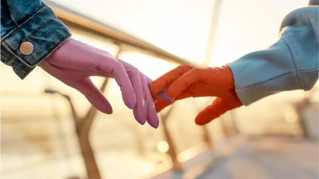 A couple walks hand in hand, but one of the persons is wearing protective gloves