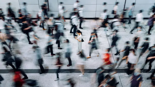 一位女性站在人行道中央，周围行人匆匆而过。