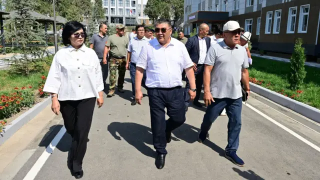 Ўқ кўйлак кийган Қамчибек Ташиев расмийлар билан бирга юриб бормоқда. 