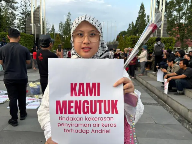 Cila menghadap kamera, sedang memegang poster bertuliskan Kami mengutuk tindakan kekerasan penyiraman air keras terhadap Andrie. 