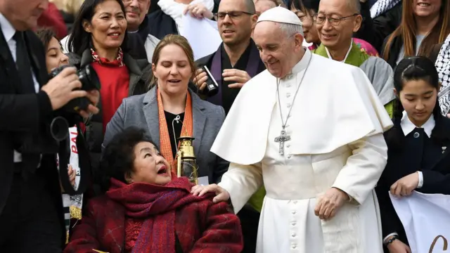 Pope Francis gently tapping the shoulders of nuclear disarmament campaigner Thurlow, who is sitting in a wheel chair
