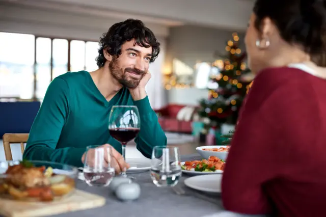 Un hombre sonríe a una mujer mientras ambos están sentados en una mesa.