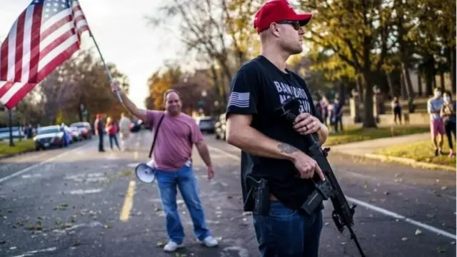 Un homme en civil avec un drapeau américain devant un autre armé