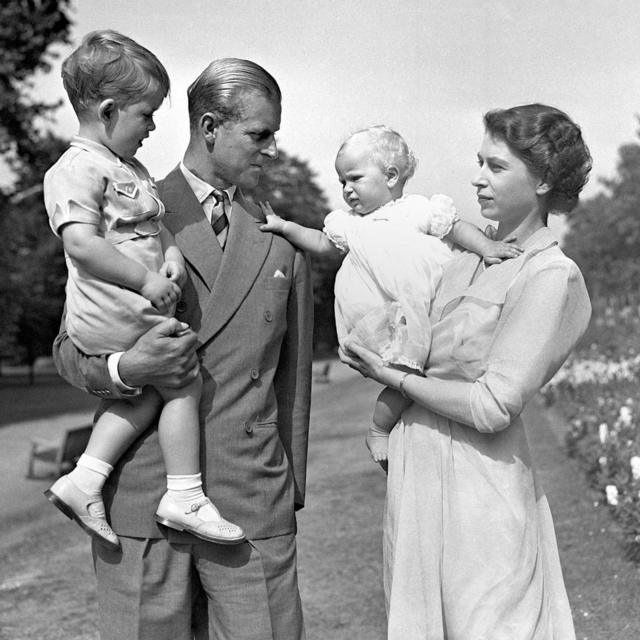 A princesa Anne nos braços da princesa Elizabeth, e o duque de Edimburgo segurando o príncipe Charles, nos jardins da Clarence House, sua residência em Londres