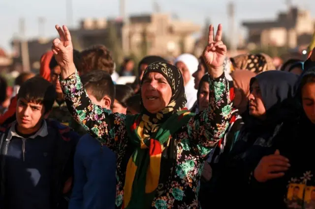 زن کرد در مراسم تشییع جسد سربازان یگان‌های مدافع خلق علامت پیروزی نشان می‌دهد