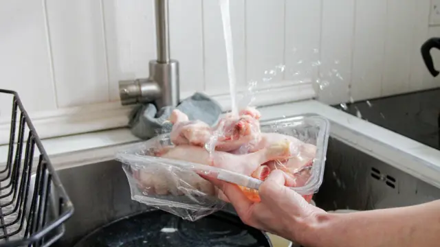 Musluk altında bir kap içindeki çiğ tavuk etlerini yıkayan bir el. 