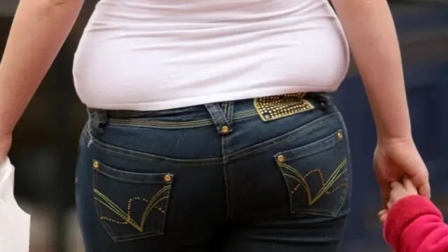 Une femme obèse tenant un enfant à la main.