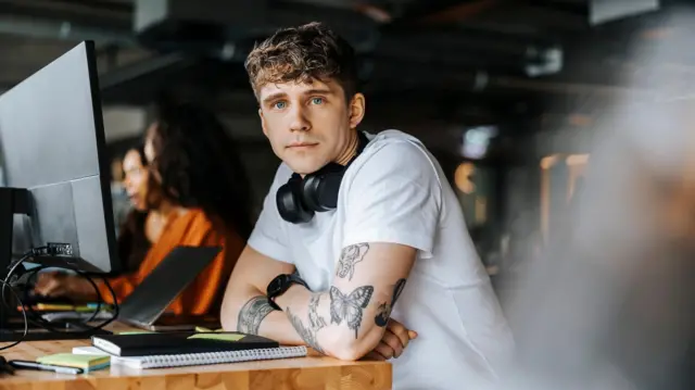 Portret młodego przedsiębiorcy opierającego się łokciami o biurko w biurze.