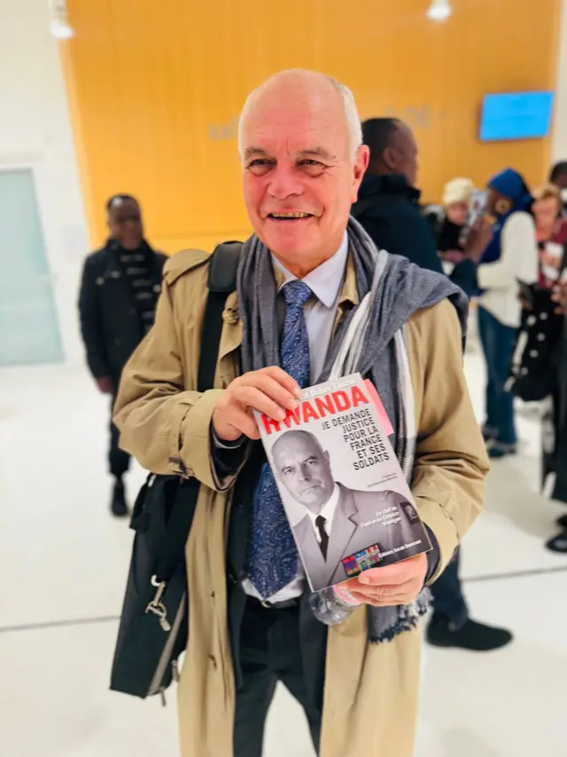 Jenerali Didier Tauzin afashe igitabo mu ntoki kiriho ifoto ye, arimo guseka 