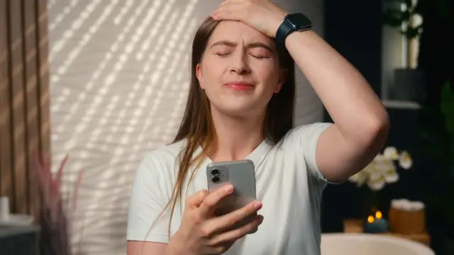 Telefonunda kumar oynayıp kaybetmiş bir kadın, üzgün bir yüz ifadesine sahip, bir elini kafasına götürmüş